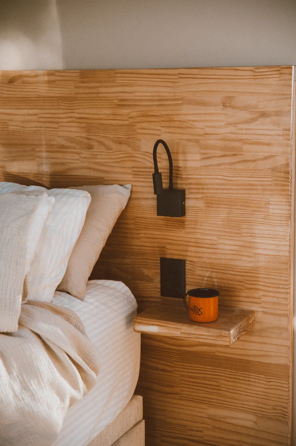 Cama com roupa de cama branca e cabeceira de madeira com luminária