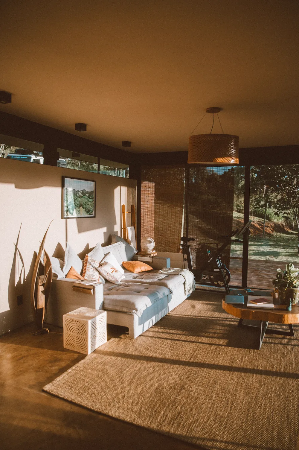 Sala com sofá claro, tapete de fibra e porta de vidro aberta para o deck