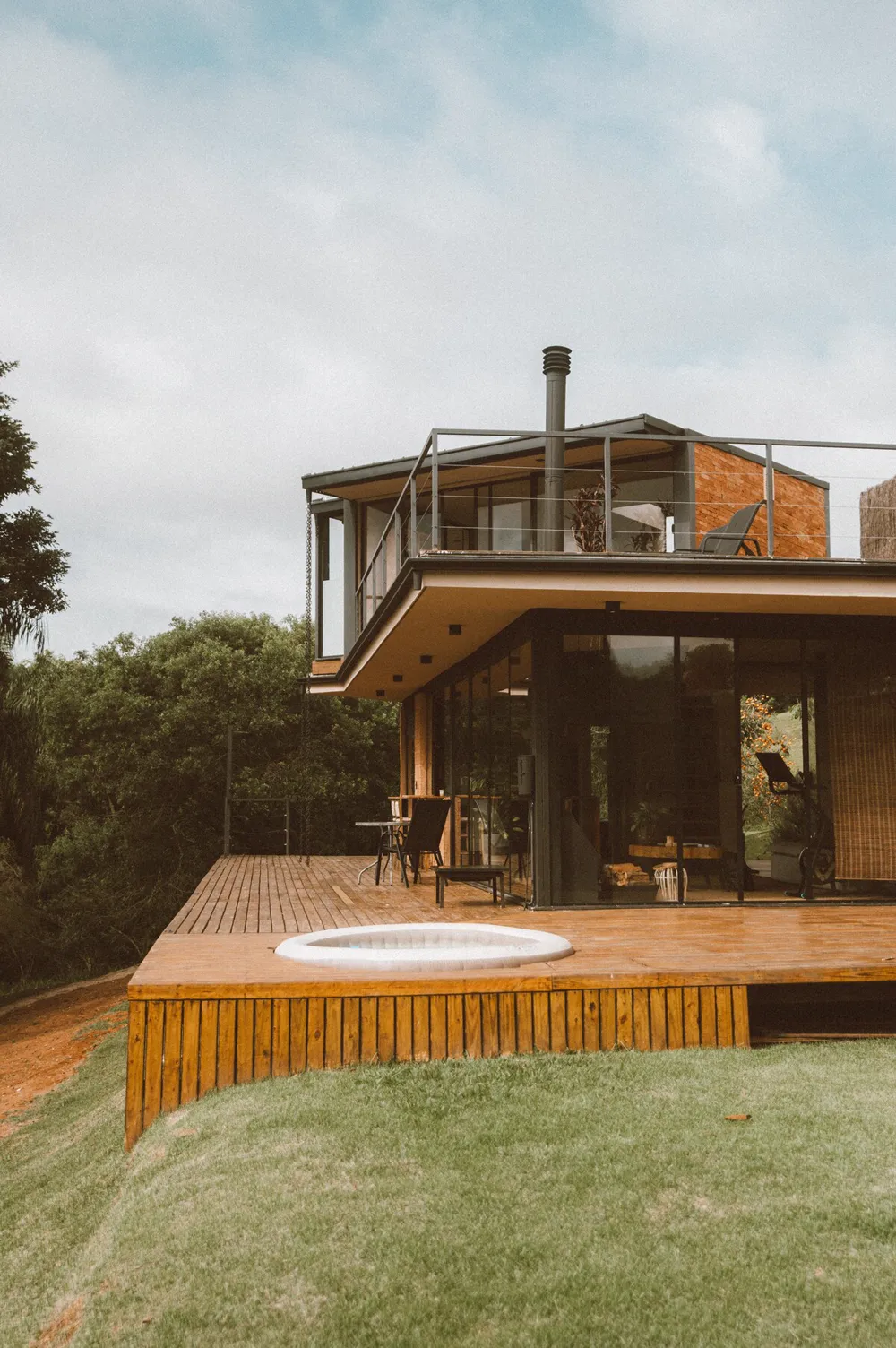 Microcasa de vidro e madeira com deck e ofurô no gramado